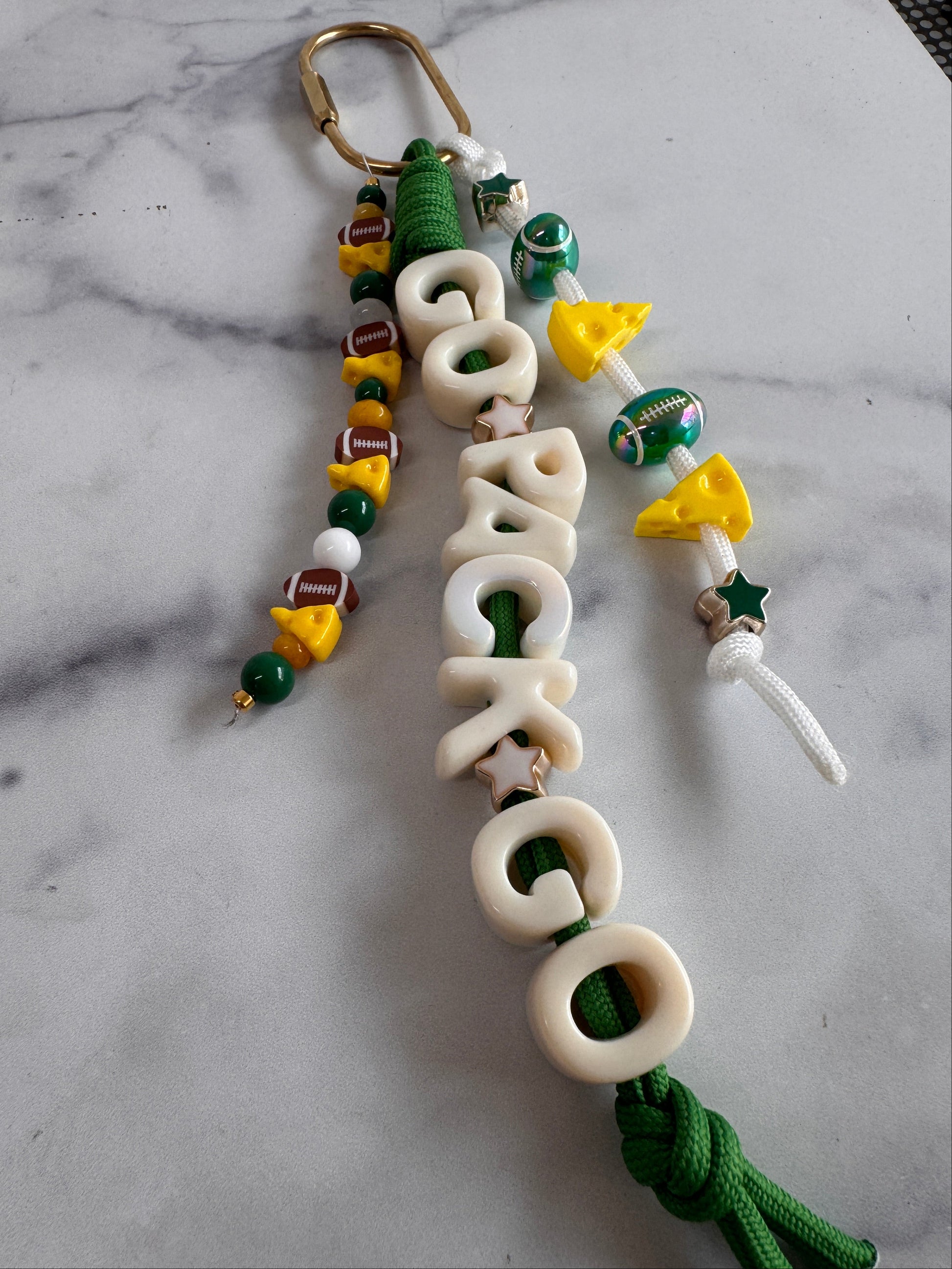 A handmade beaded keychain or carabiner charm inspired by the Green Bay Packers. Green paracord features the words "Go Pack Go", the rally cry for the Green Bay packers